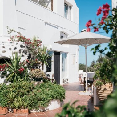 Sunlit Santorini villa with white architecture and vibrant garden, perfect for relaxing outdoors.